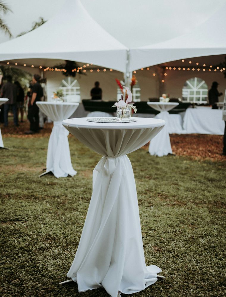 White canopy tents on a green lawn, with cocktail tables draped in white linen