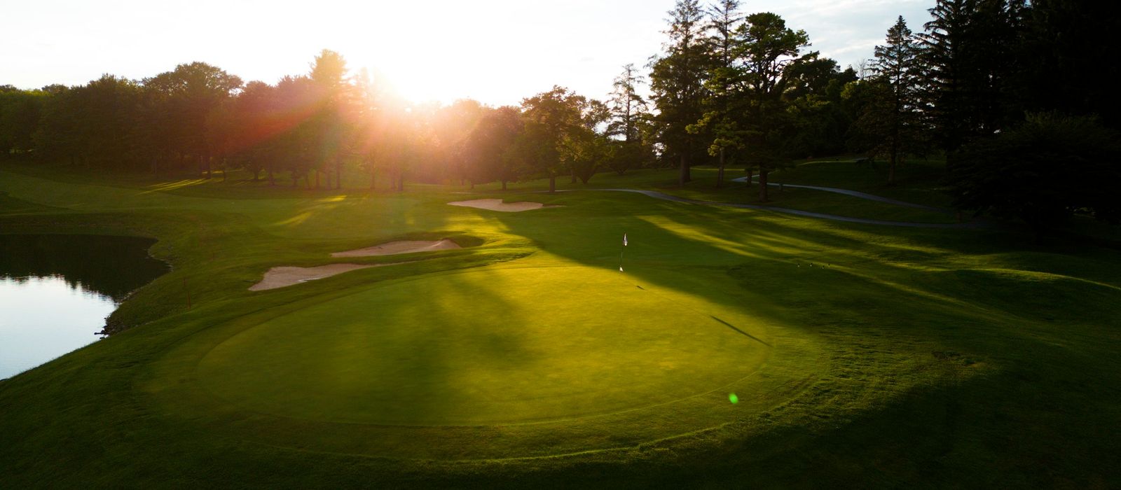 Low evening sun over a golf green, with long shadows, bunkers, and a line of trees