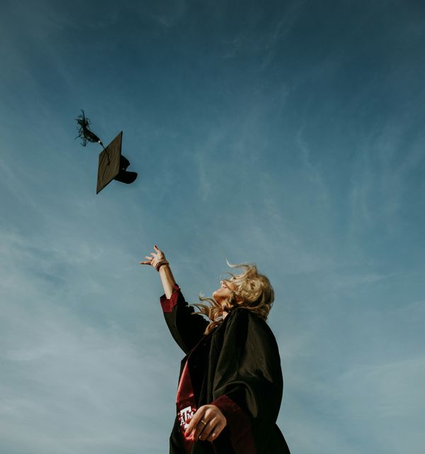 A graduate in a gown tossing a cap into an evening sky