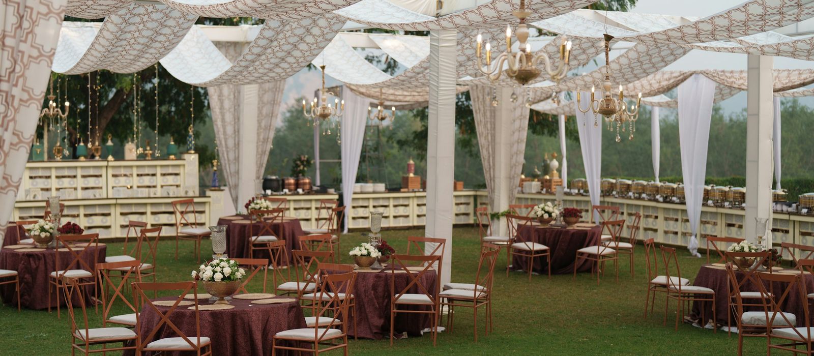 An outdoor reception on a lawn under white draped canopies, with tables set for dinner