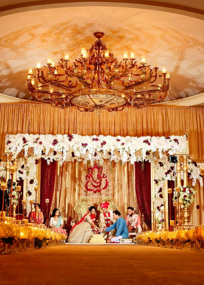 A couple at their wedding ceremony under a floral canopy beneath a chandelier