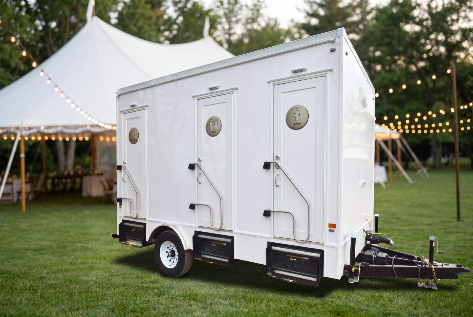 Luxury washroom trailer at an outdoor wedding venue at dusk with a marquee tent and string lights
