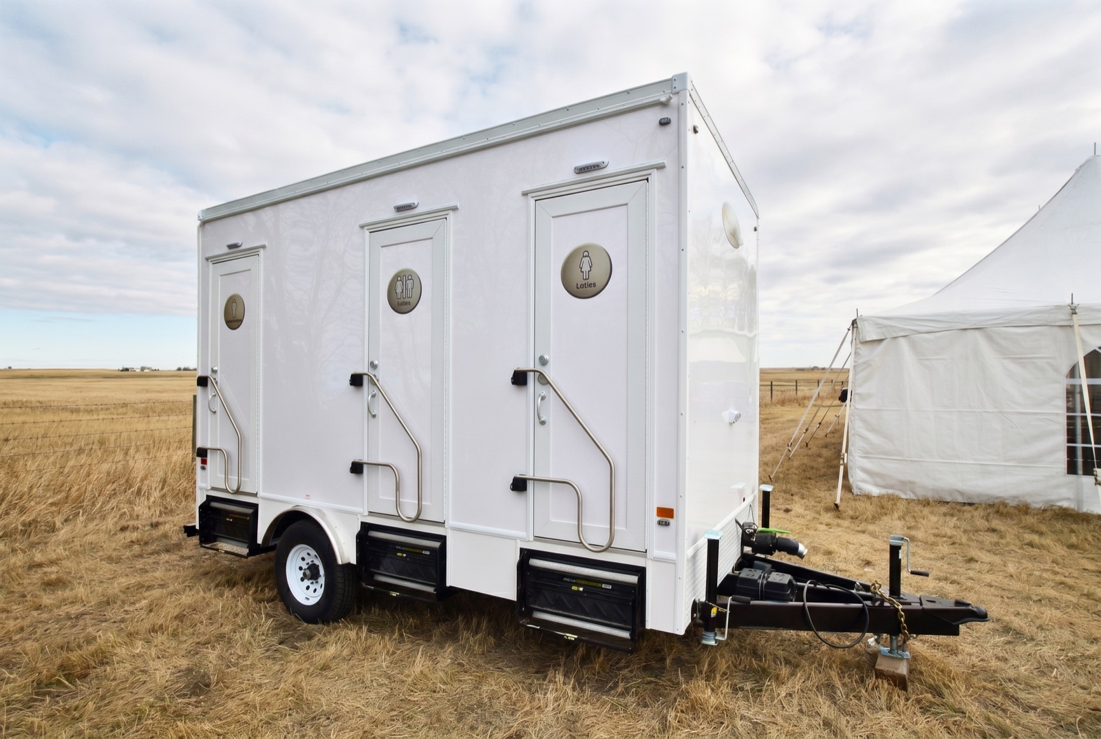 Luxury washroom trailer in a prairie farm field beside a white event tent in the Alberta foothills