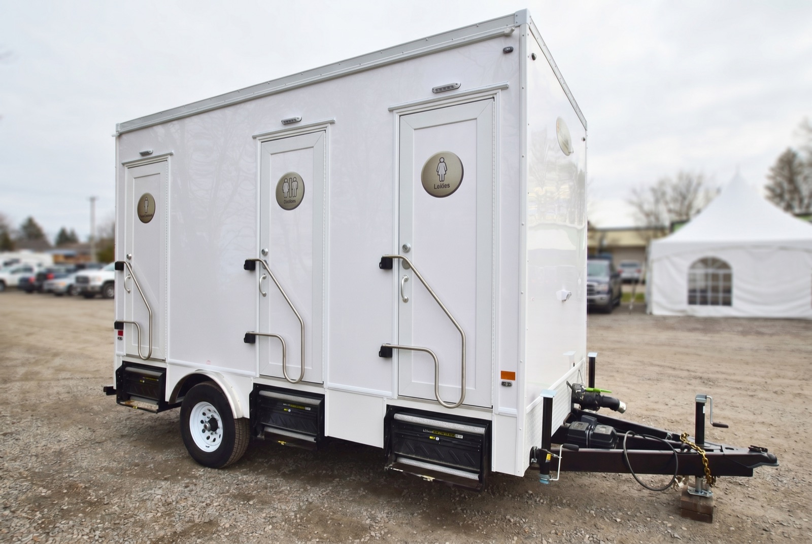 Luxury washroom trailer on a lot at an outdoor community event with a marquee tent
