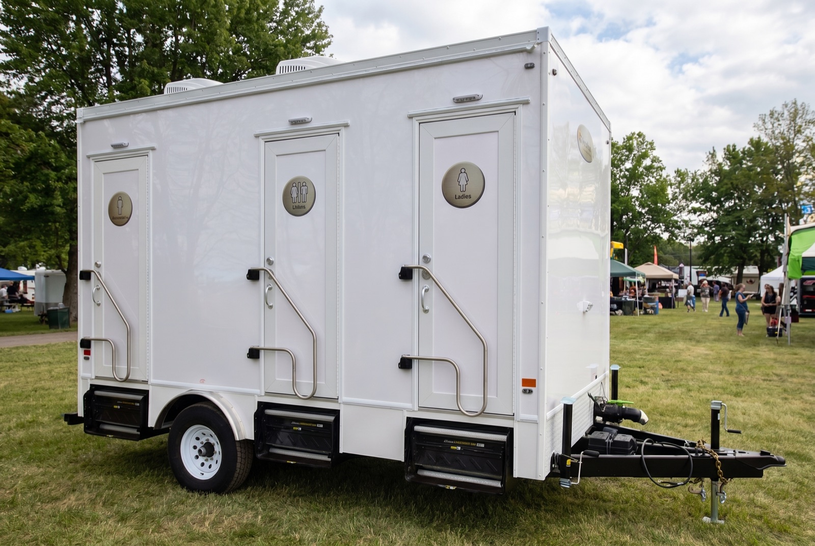 Luxury washroom trailer on grass at an outdoor event with vendor tents