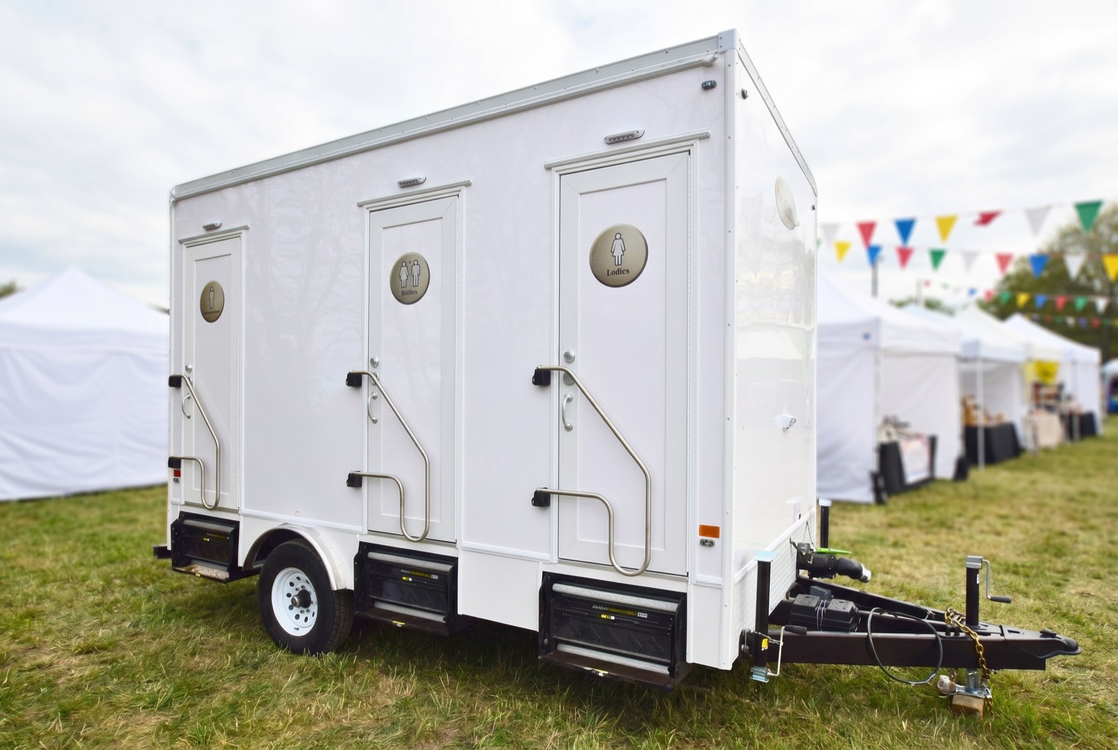 Luxury washroom trailer at an outdoor summer festival with vendor tents and bunting
